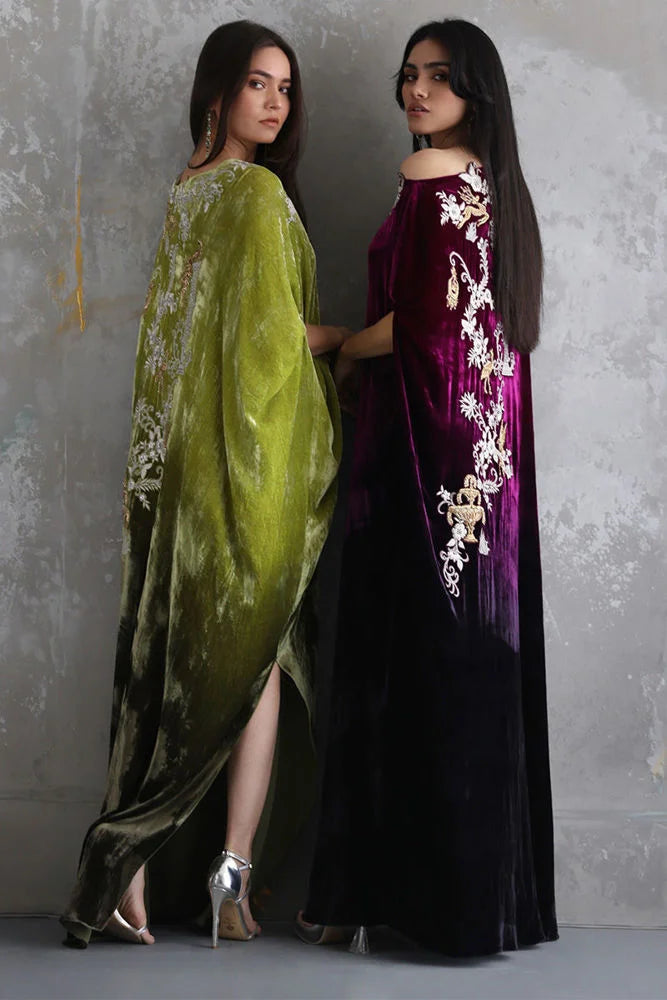 Two women wearing elegant dresses with floral embroidery against a textured wall.