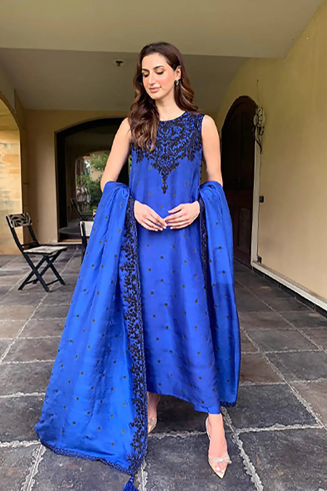 Woman in a blue traditional outfit with intricate designs standing outdoors.