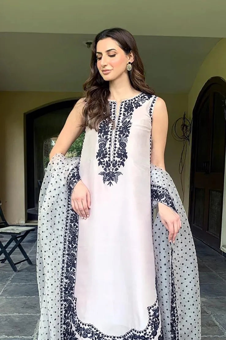 Woman wearing a white and black embroidered traditional outfit indoors.