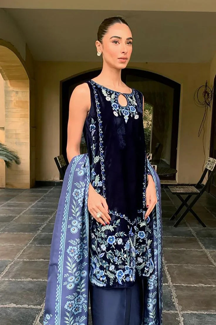 Woman in a blue embroidered traditional outfit standing in an outdoor setting.