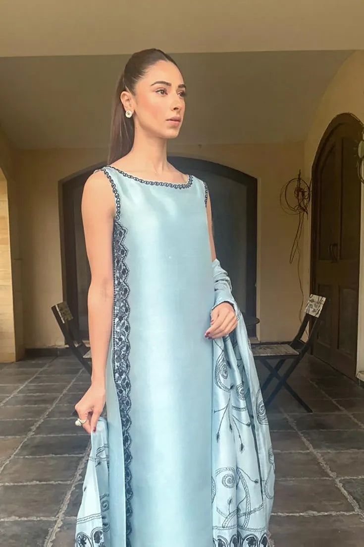 Woman in a light blue dress with intricate patterns standing indoors.