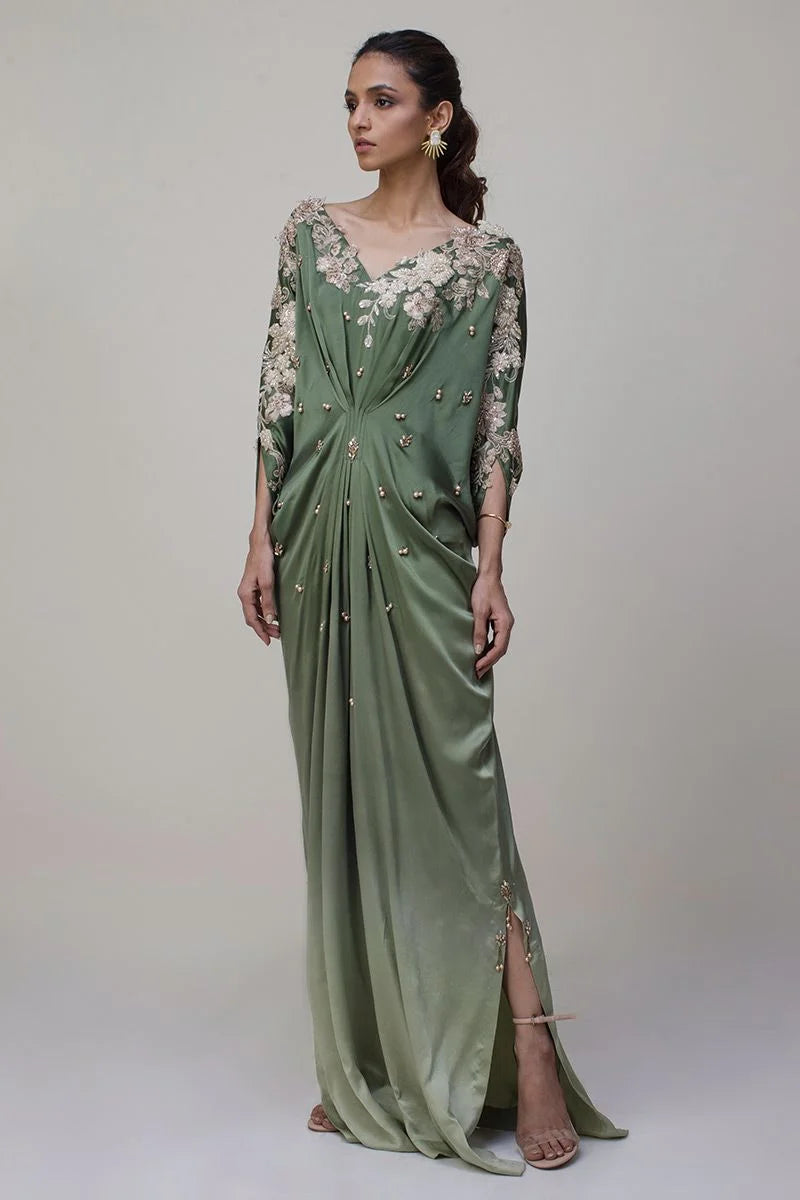 Woman wearing a green evening gown with floral embellishments on a plain background