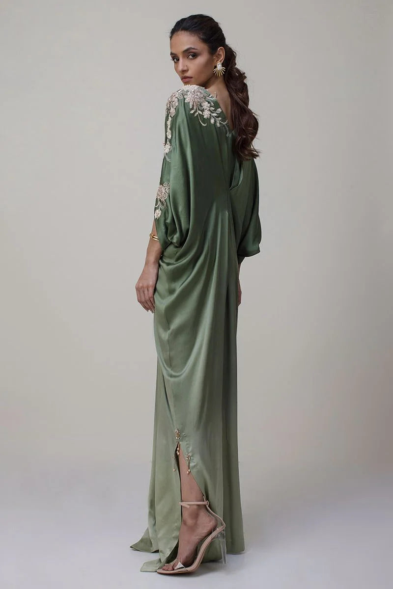 Woman wearing a green evening gown with floral embroidery on a plain background