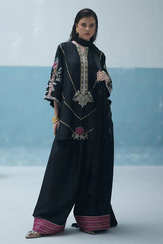 Woman wearing a black traditional outfit with intricate embroidery against a light blue background