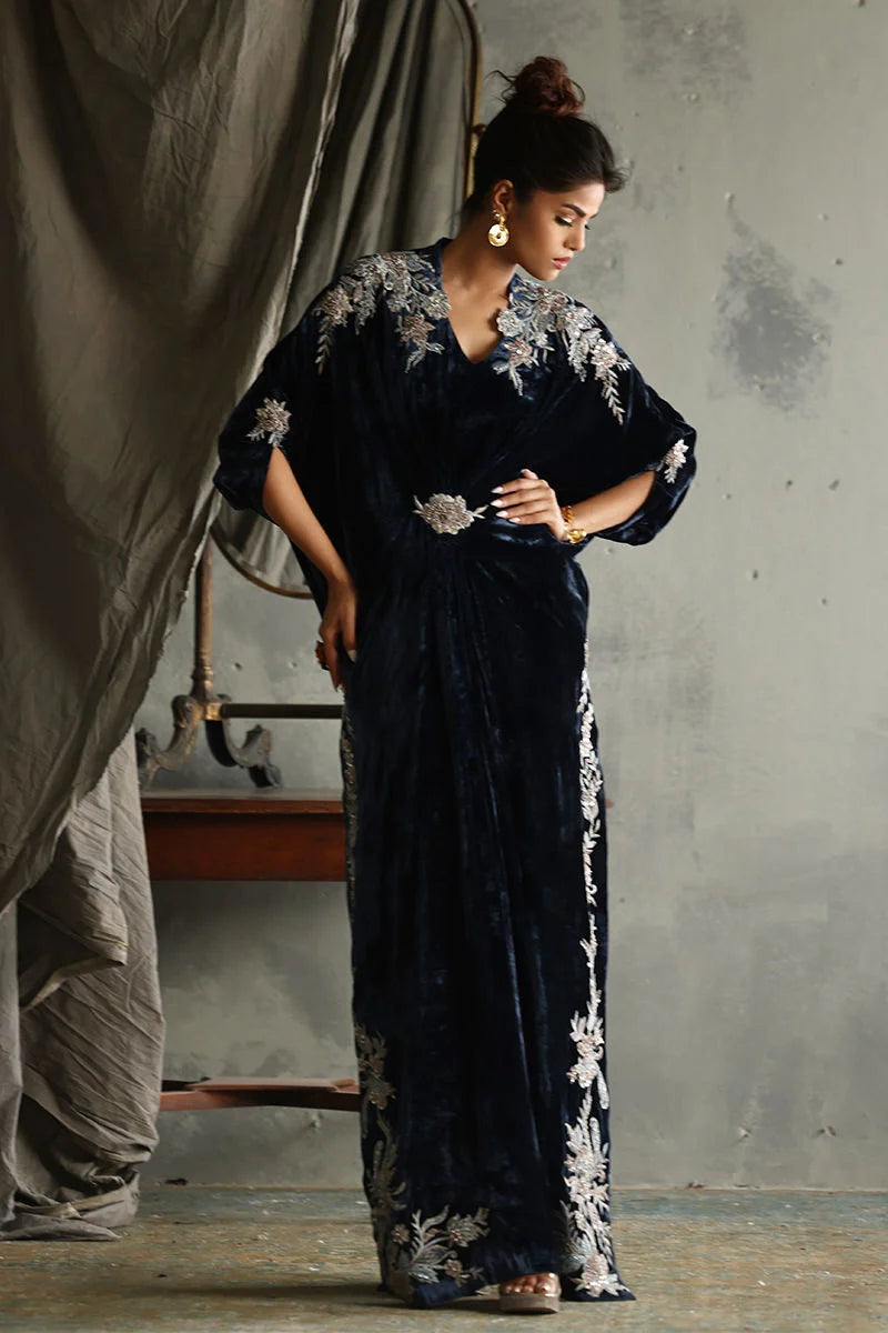 Woman wearing a dark blue saree with white floral embroidery in a rustic setting.