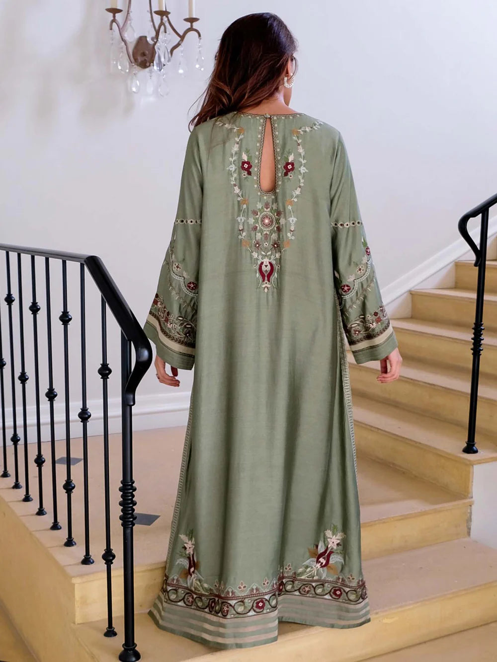 Woman wearing a green embroidered dress standing on a staircase.