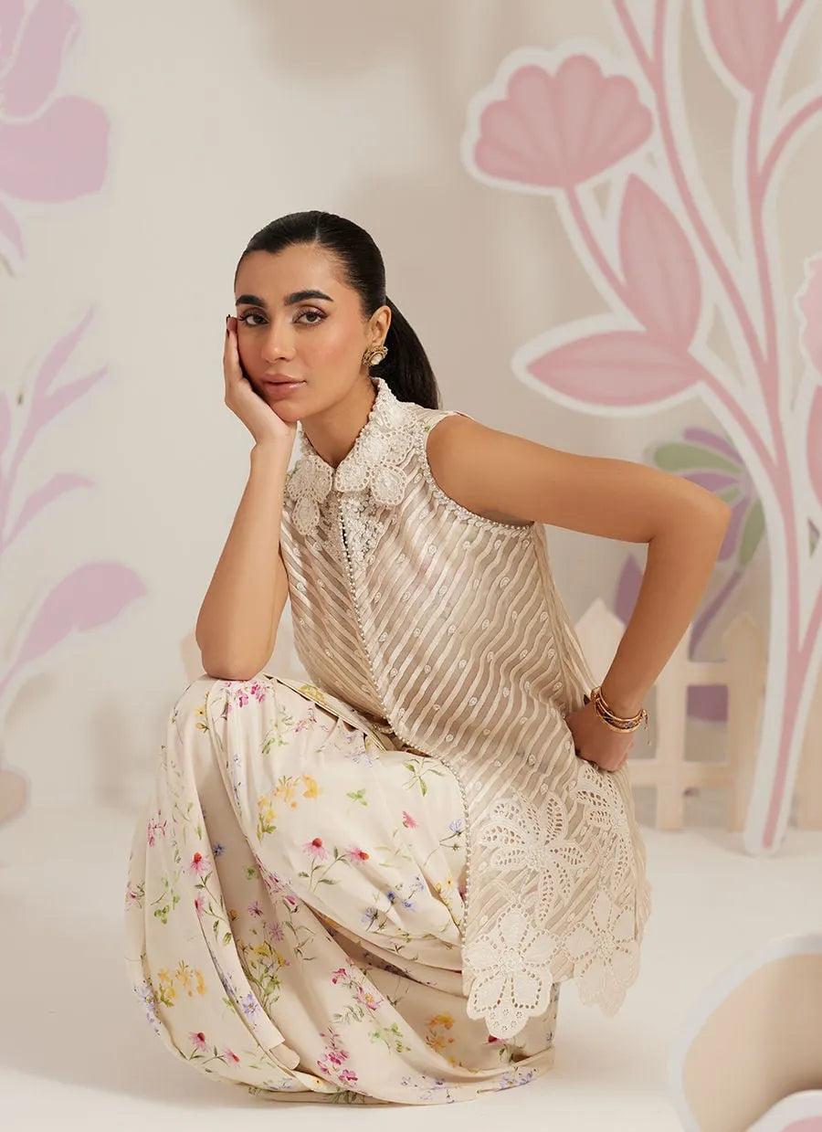 Woman in a floral dress sitting against a decorative wall with pink and purple floral patterns.