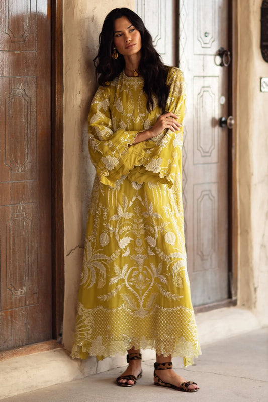 Woman in a yellow embroidered dress standing in front of a wooden door.