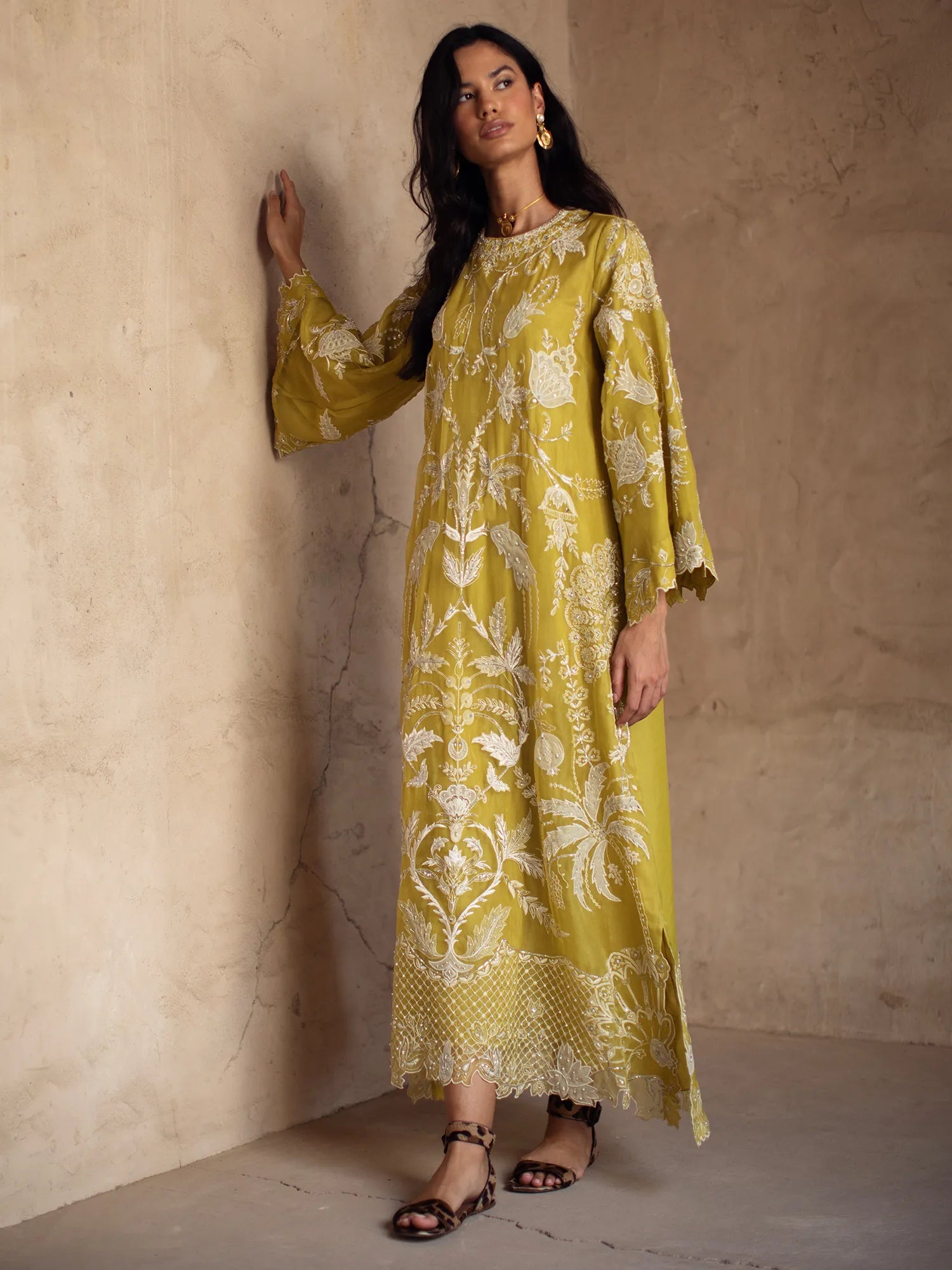 Woman wearing a yellow patterned dress against a beige wall.