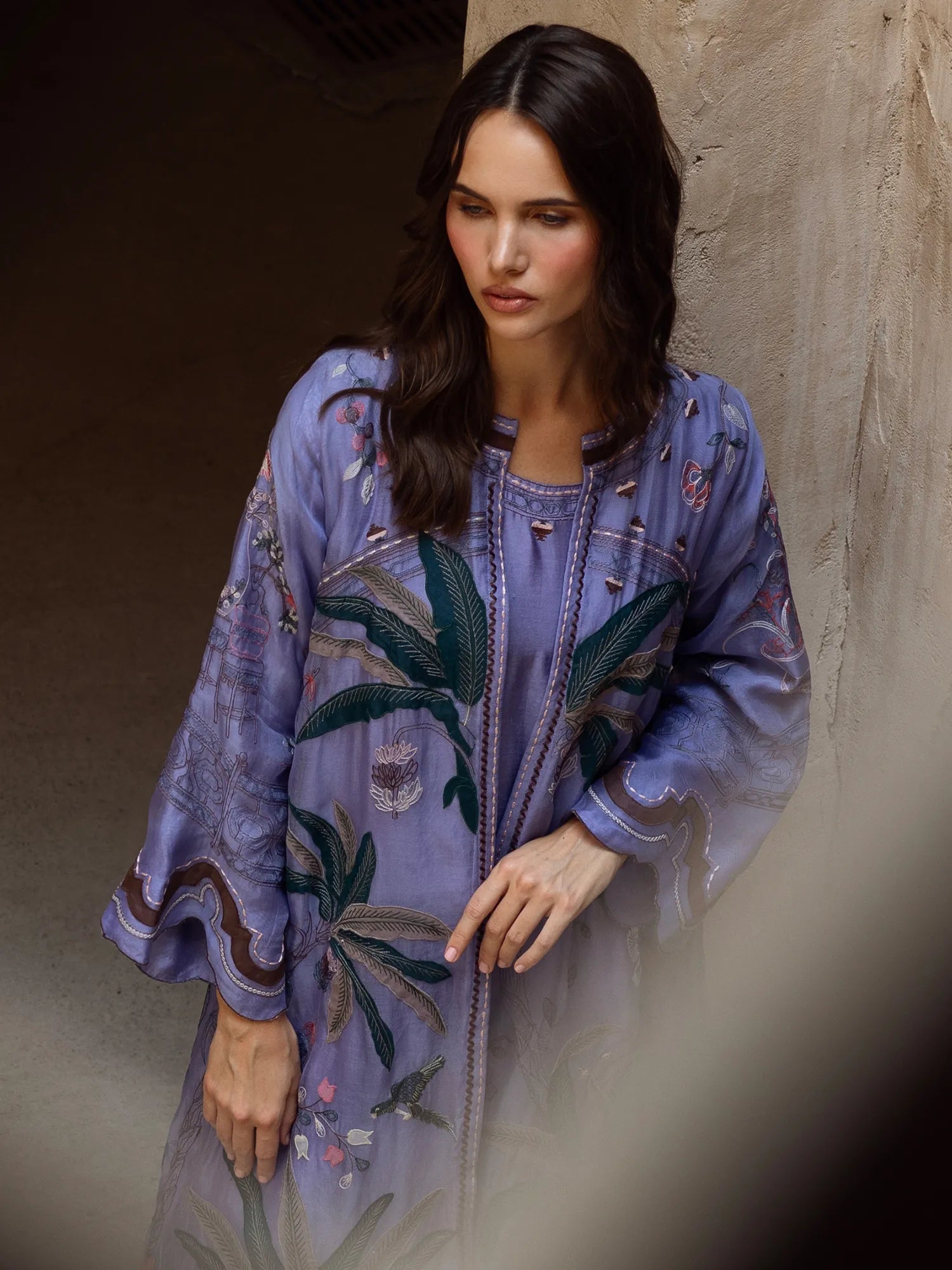 Woman wearing a purple embroidered dress against a textured wall.