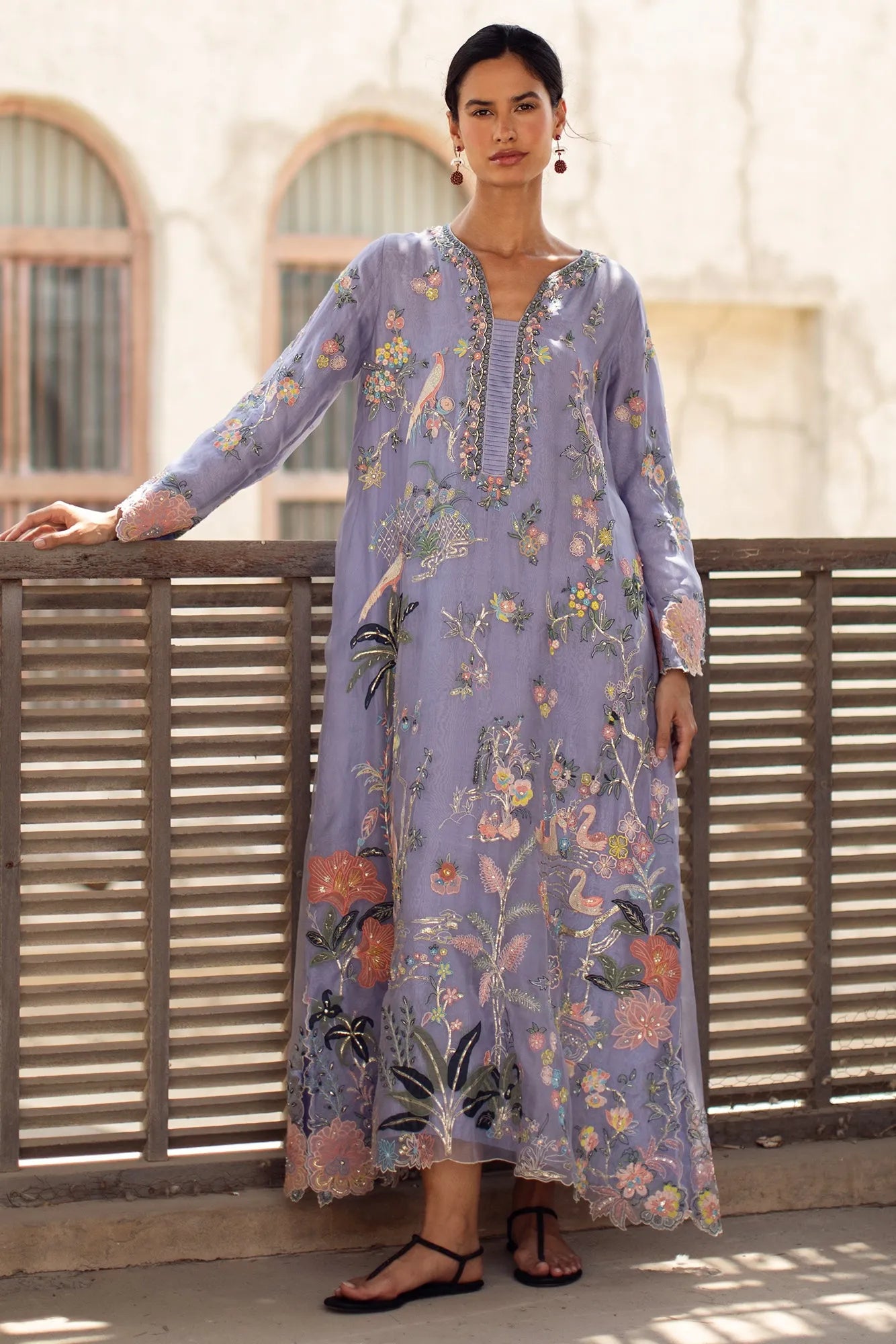 Woman wearing a floral embroidered dress standing on a balcony.