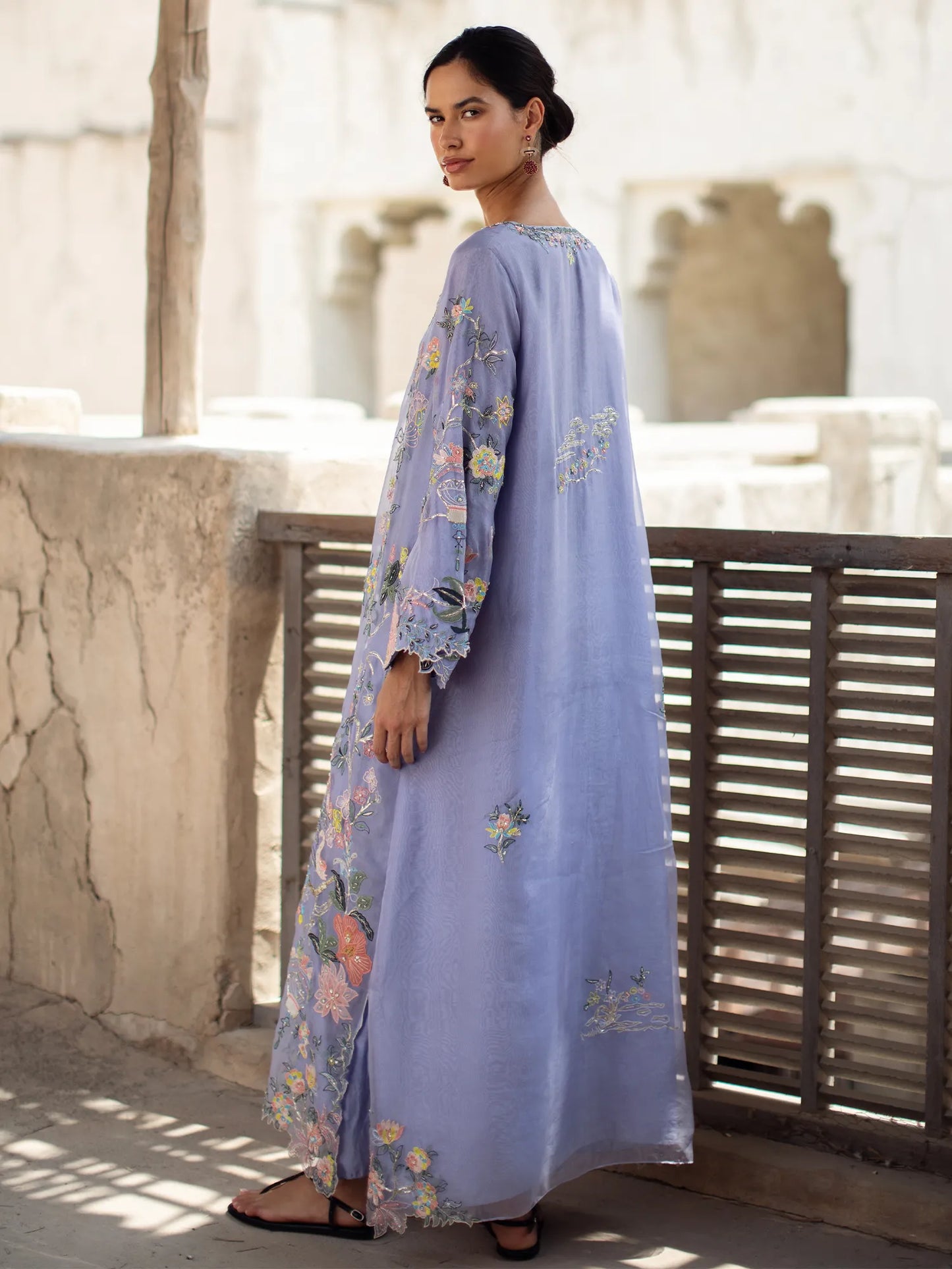 Woman wearing a long, light blue embroidered dress standing outdoors.