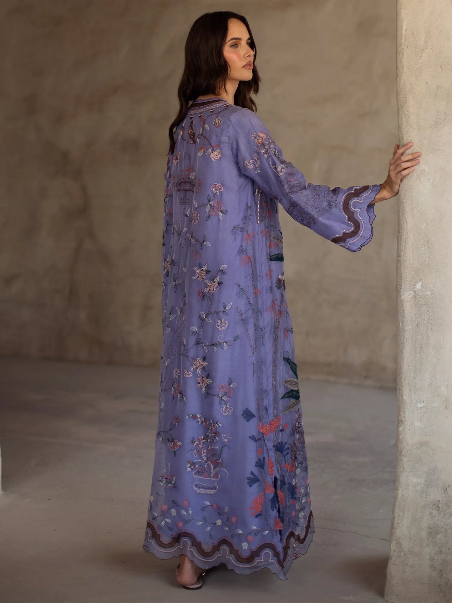 Woman wearing a long, embroidered purple dress against a neutral wall.