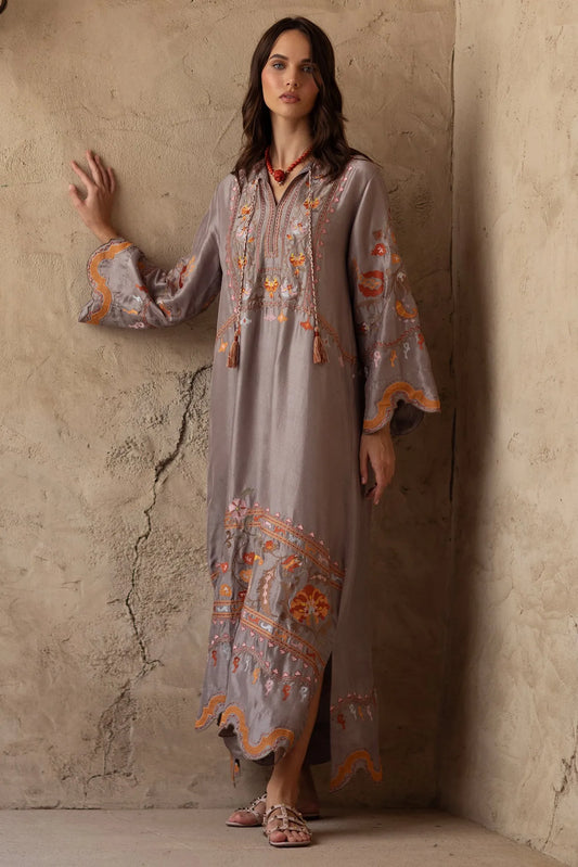 Woman wearing a long, embroidered dress against a textured wall.