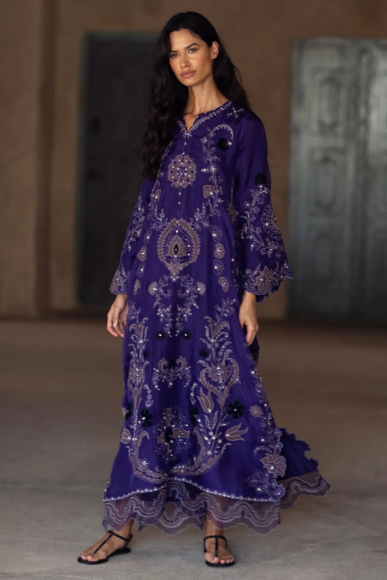 Woman wearing a purple embroidered dress with a textured wall background