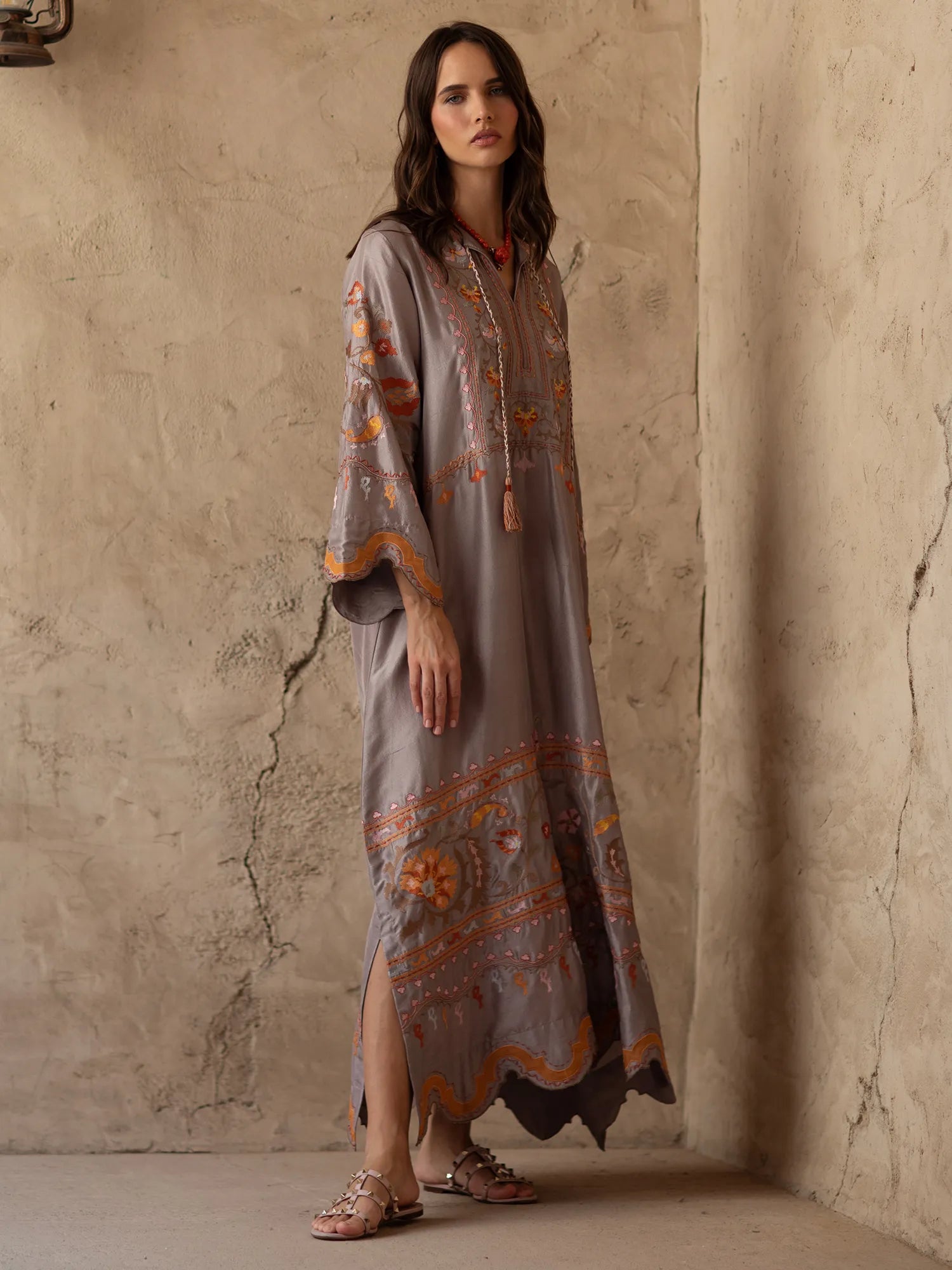 Woman wearing a long, patterned dress against a textured wall.