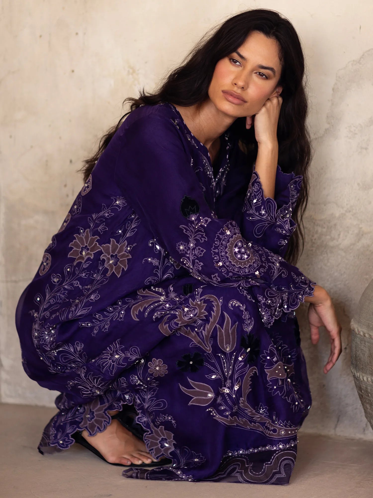 Woman wearing a purple embroidered outfit sitting against a neutral background