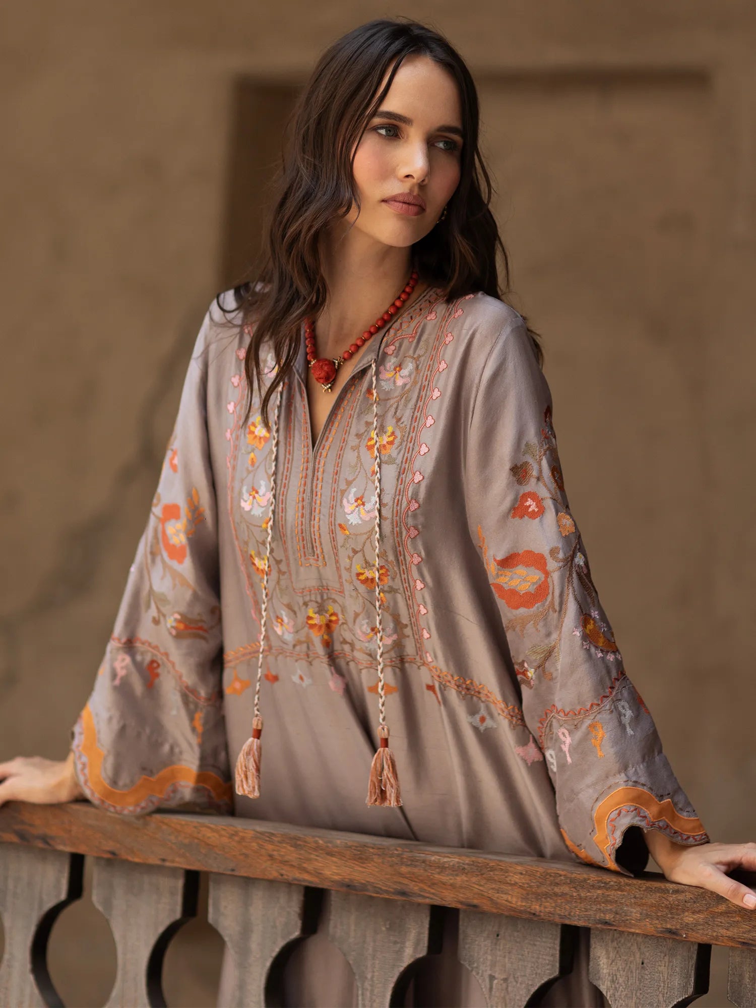Woman wearing a beige embroidered blouse with orange details, standing against a neutral background.