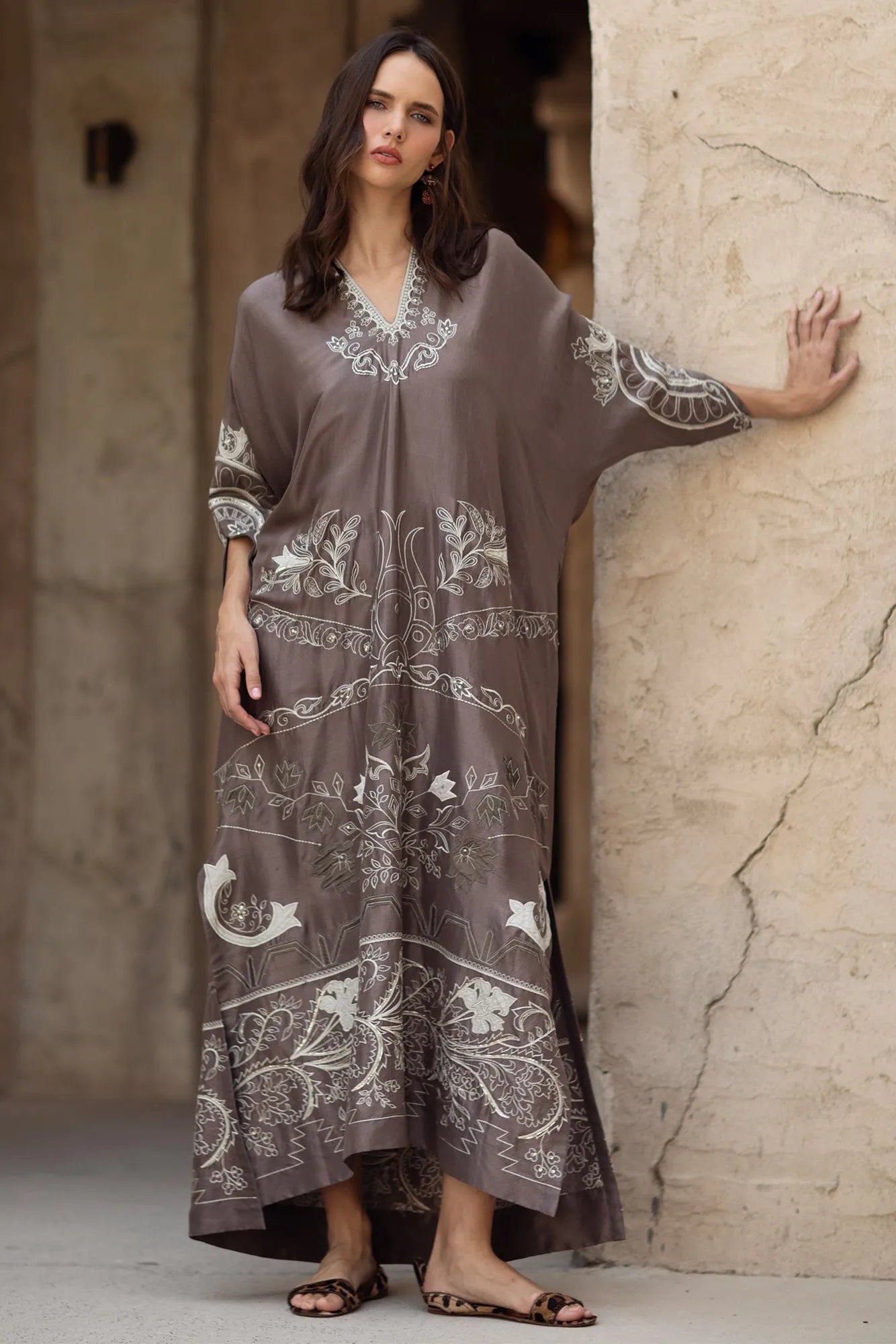Woman wearing a long, patterned dress against a textured wall.