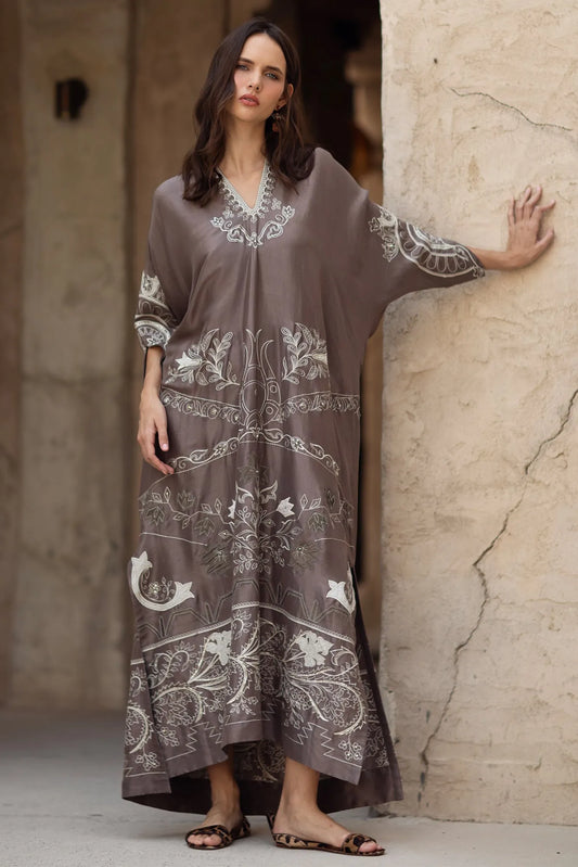 Woman wearing a long, patterned dress against a textured wall.