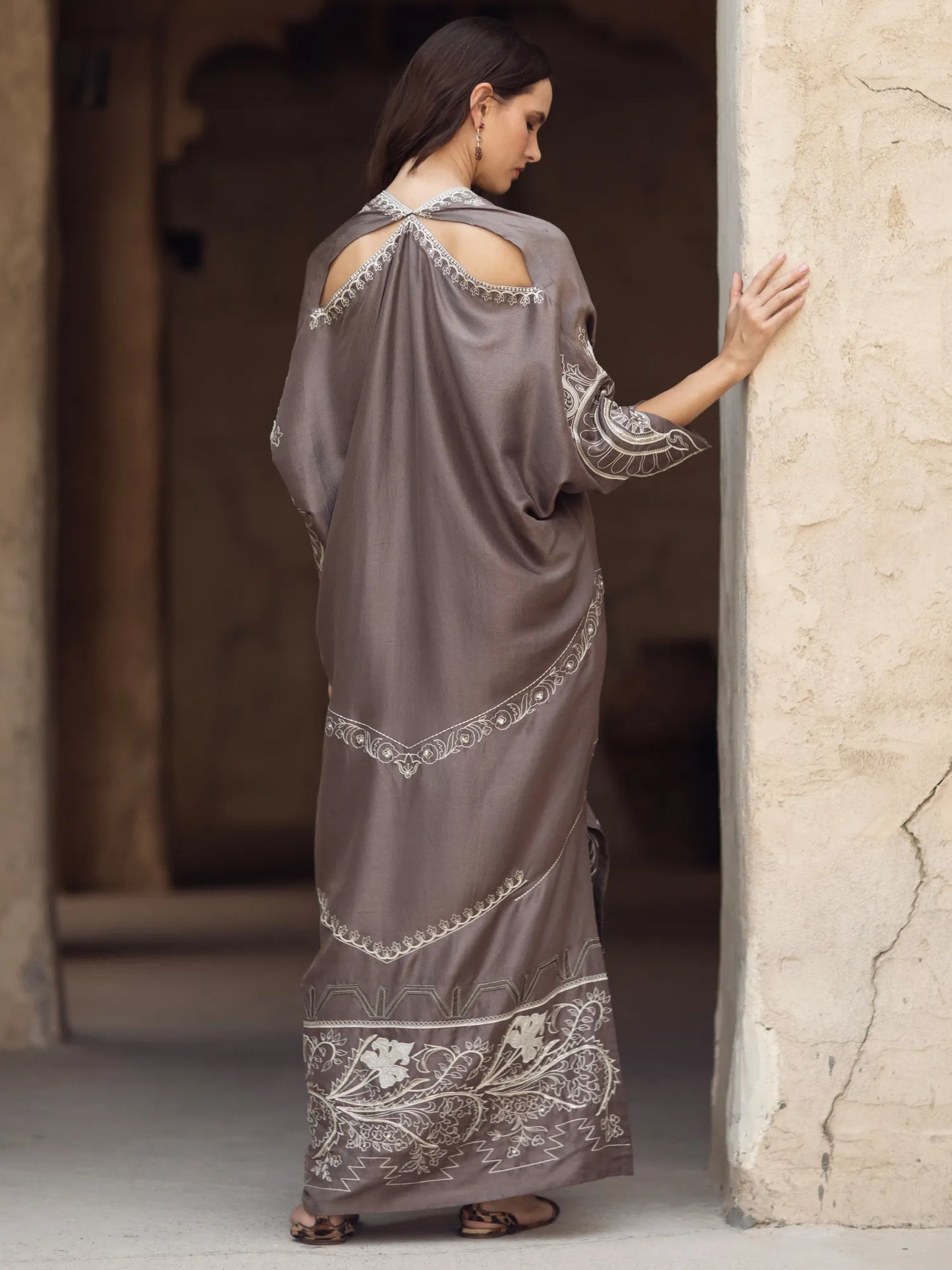 Woman in a long, elegant dress with intricate patterns standing in a stone archway.
