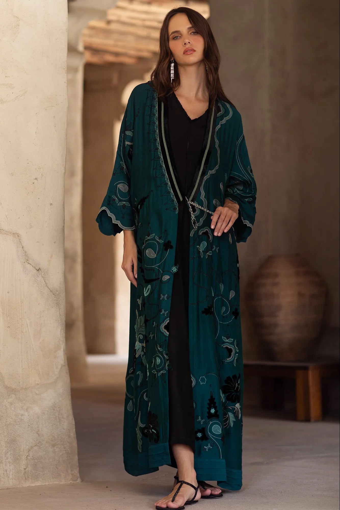 Woman wearing a long teal embroidered dress in an indoor setting.