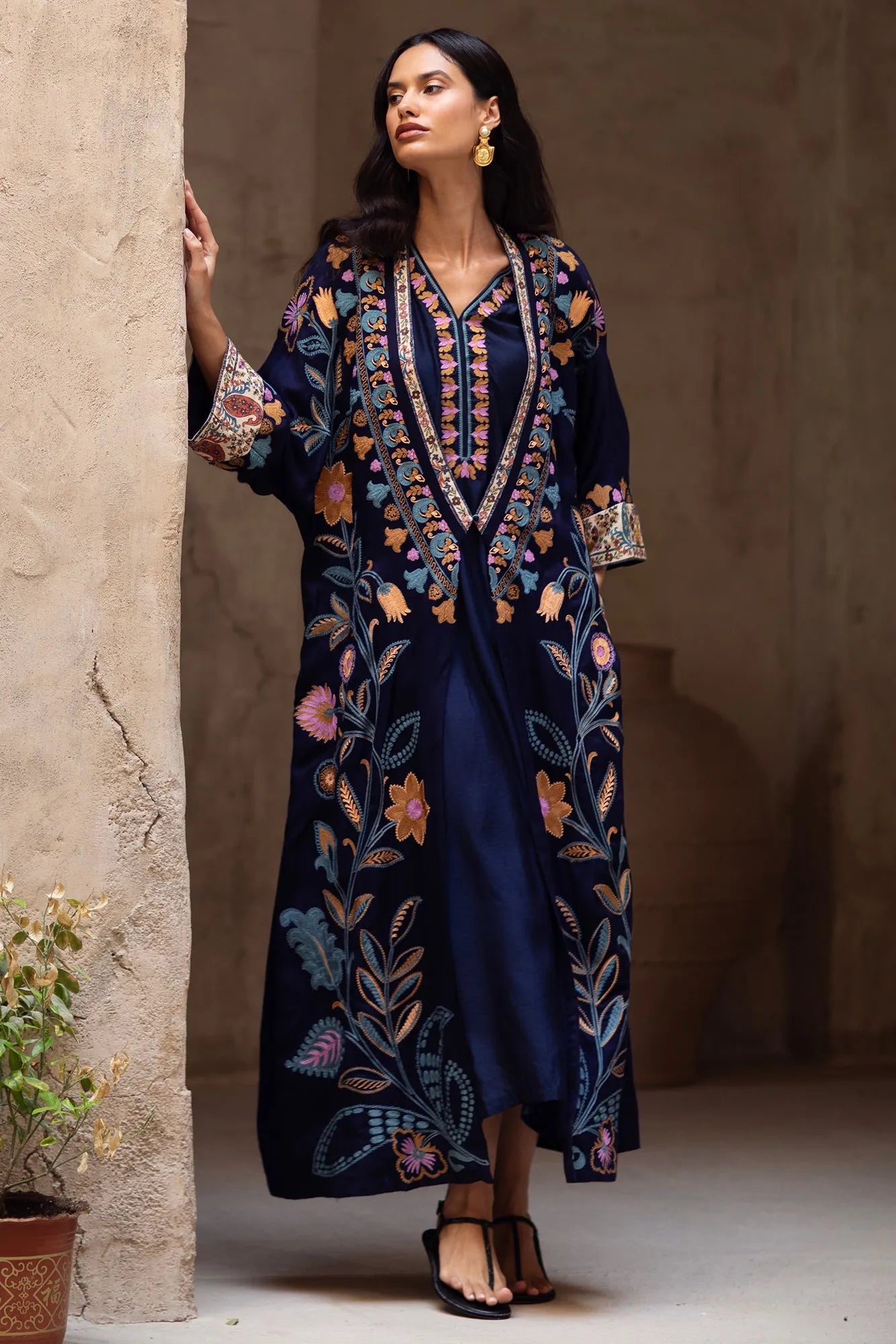 Woman wearing a dark blue embroidered dress standing against a textured wall.