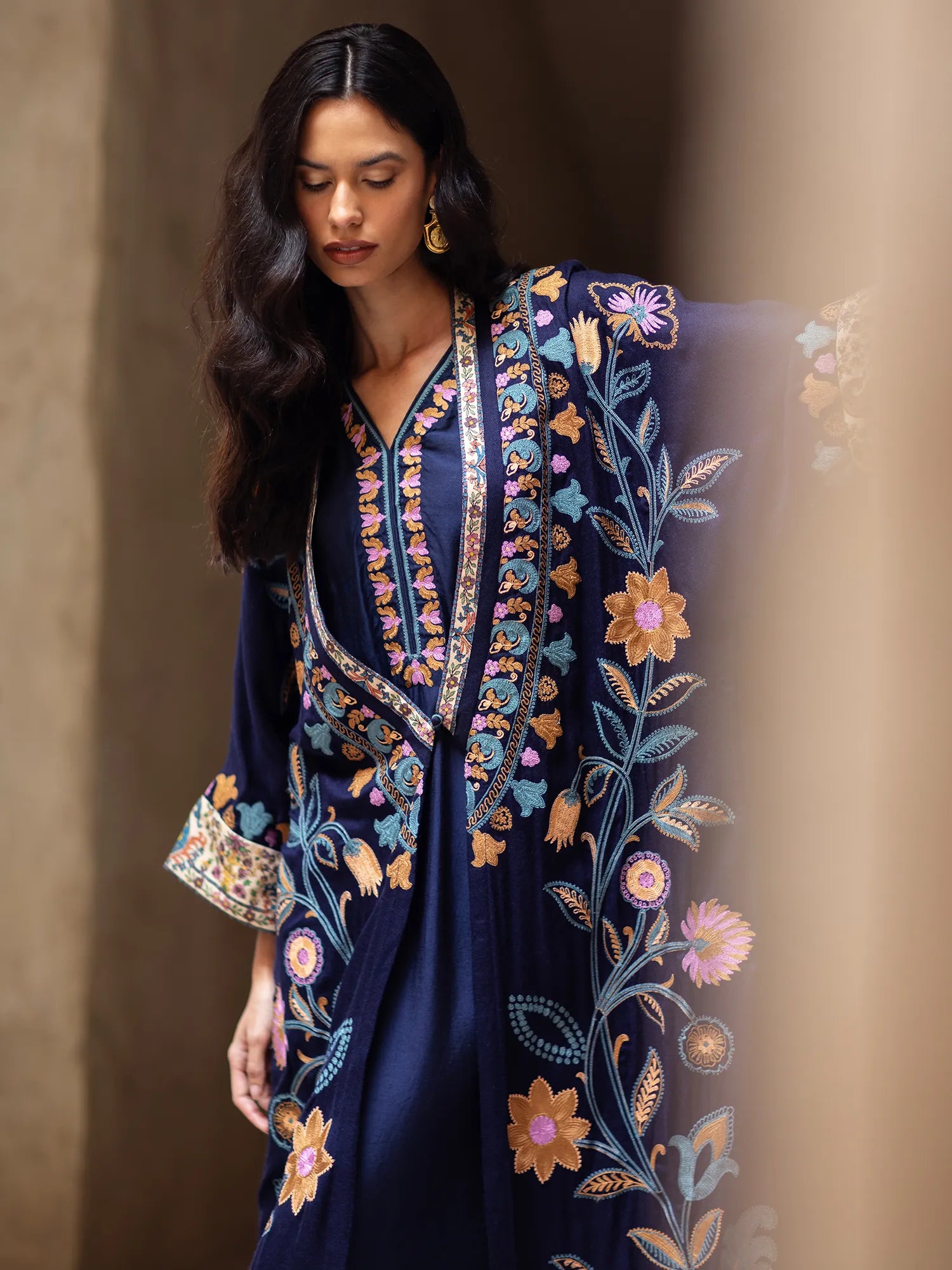 Woman wearing a navy blue dress with intricate floral embroidery against a brown background