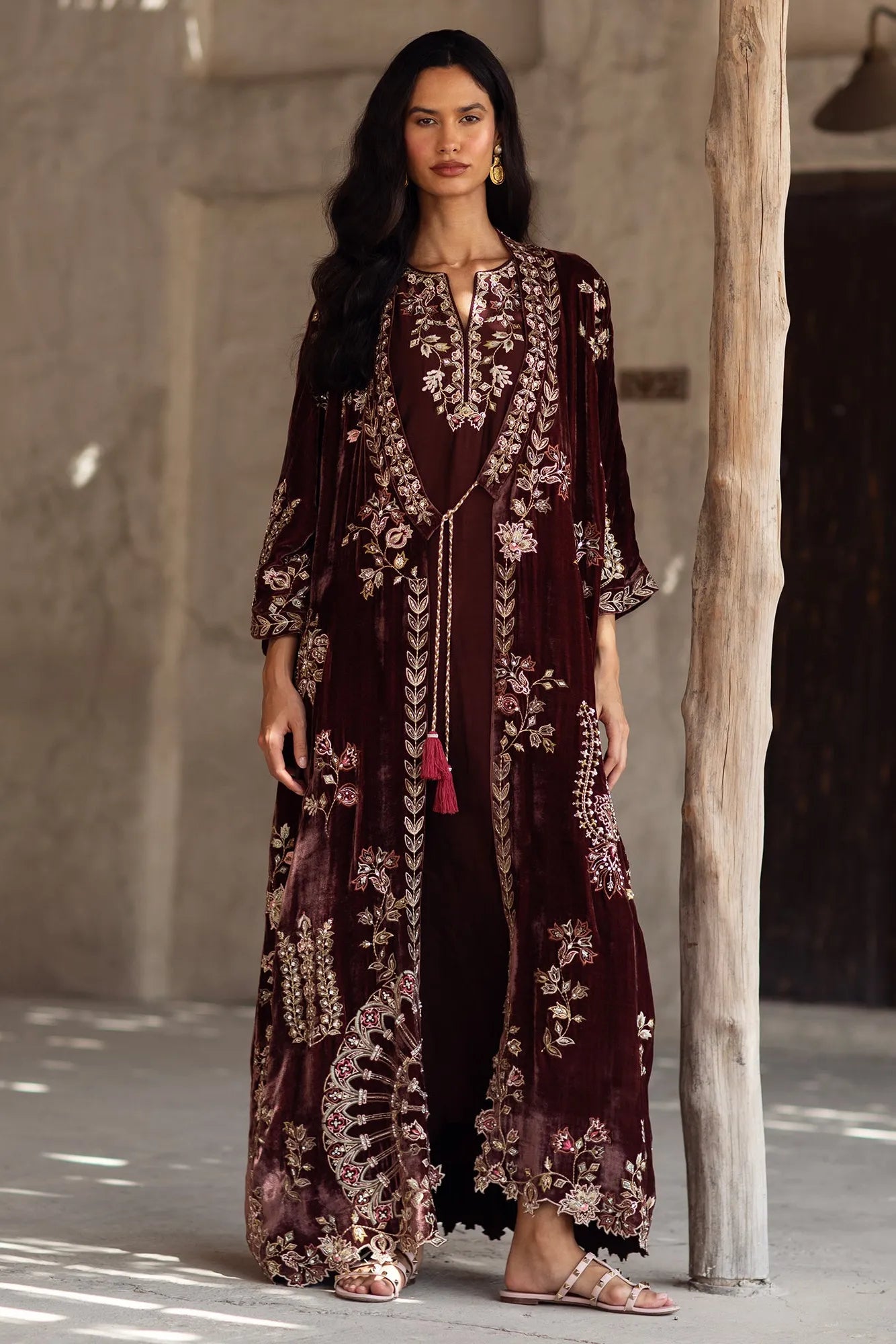 Woman wearing a long, dark brown embroidered dress with a neutral background