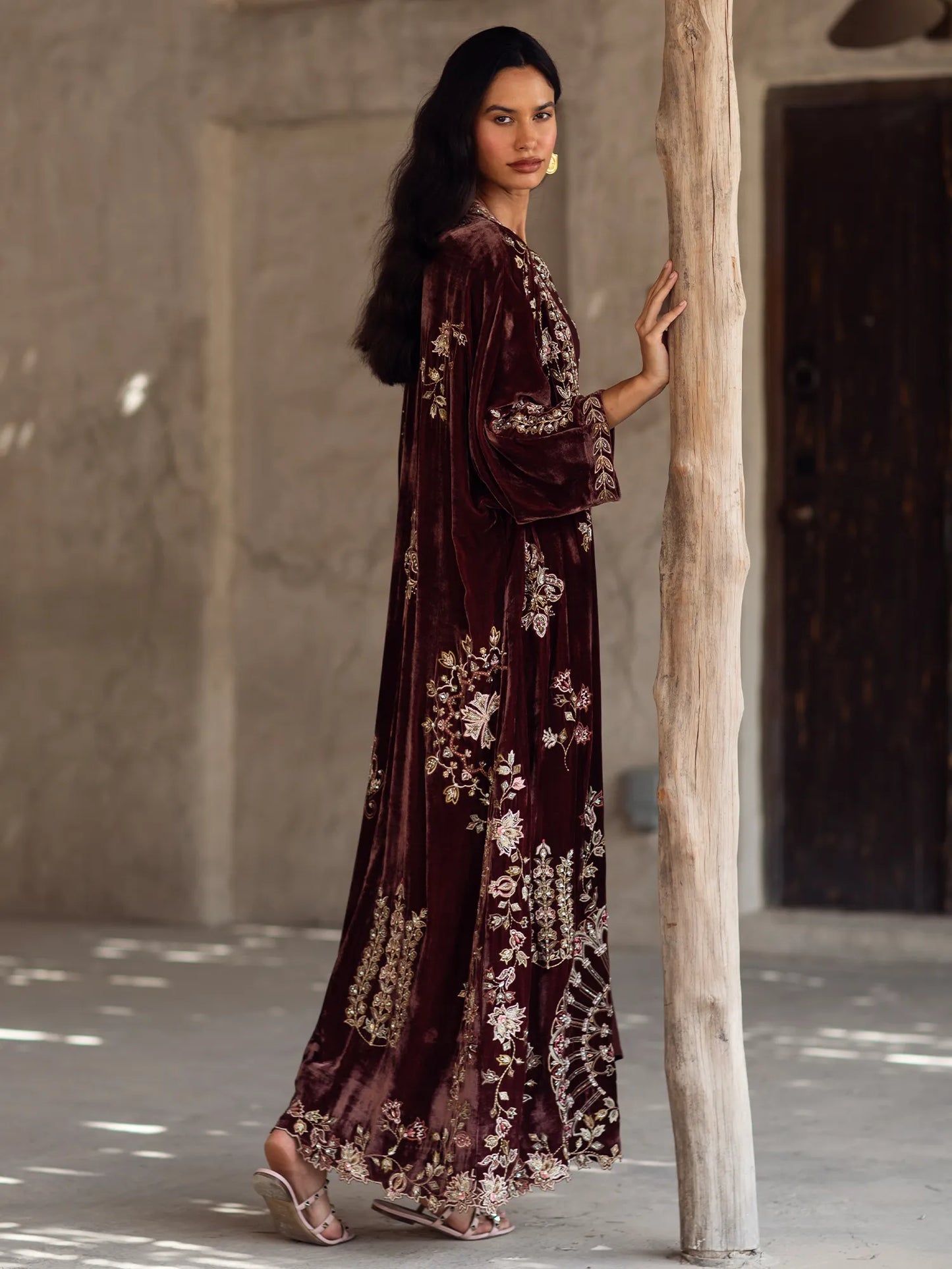 Woman in a long, dark brown floral dress standing against a textured wall.