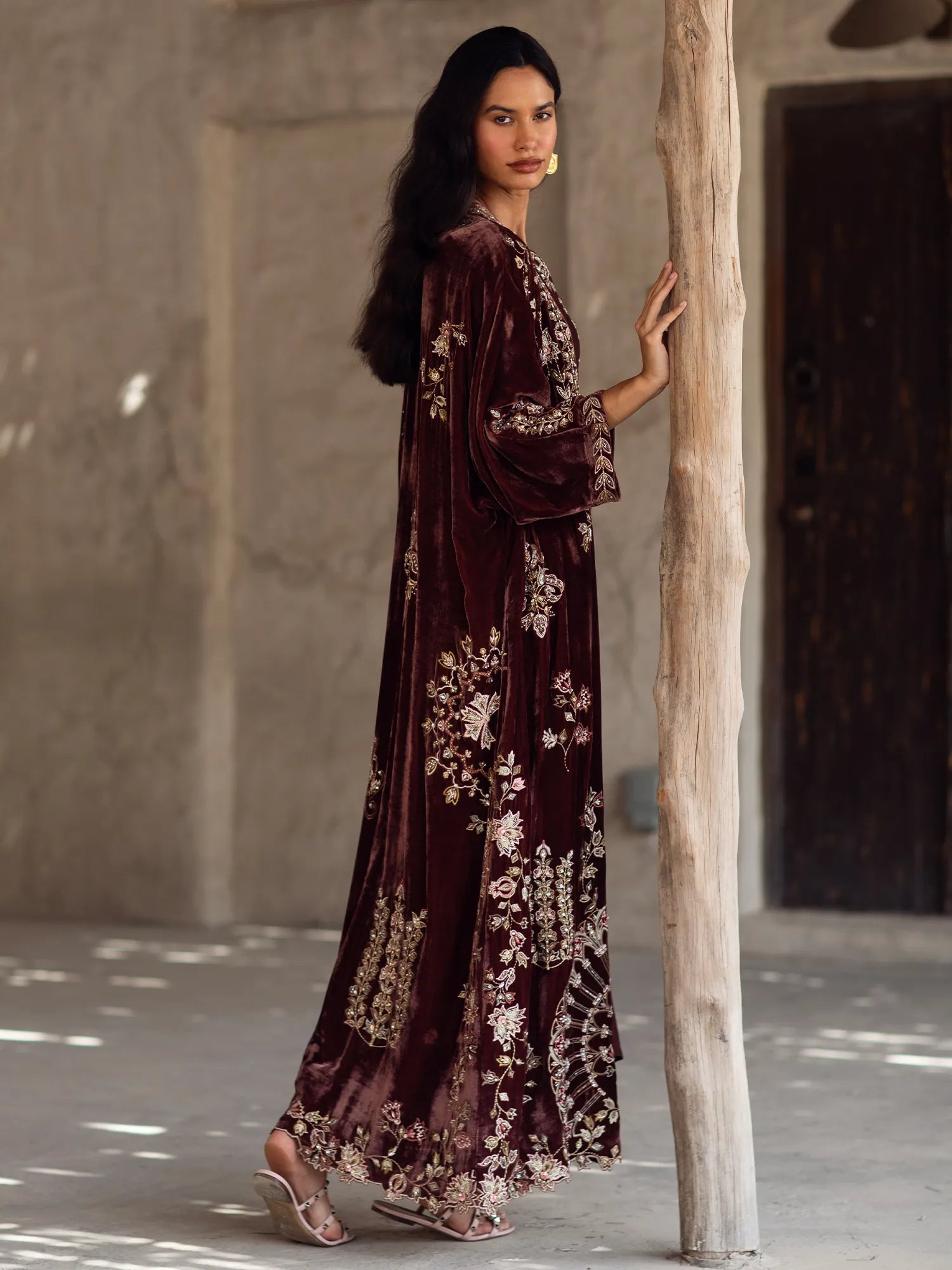 Woman in a long, dark brown floral dress standing against a textured wall.