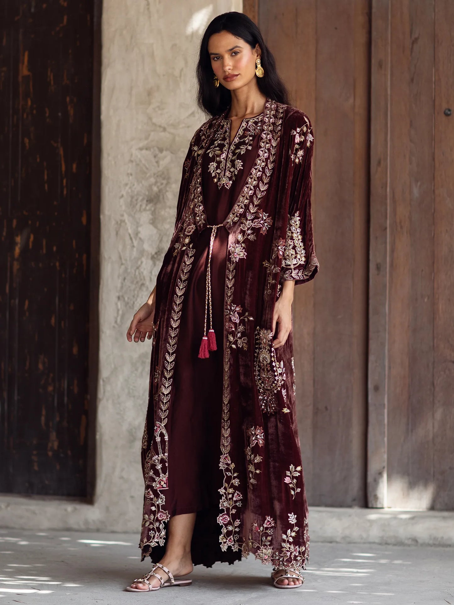 Woman wearing a burgundy embroidered dress with a wooden door in the background
