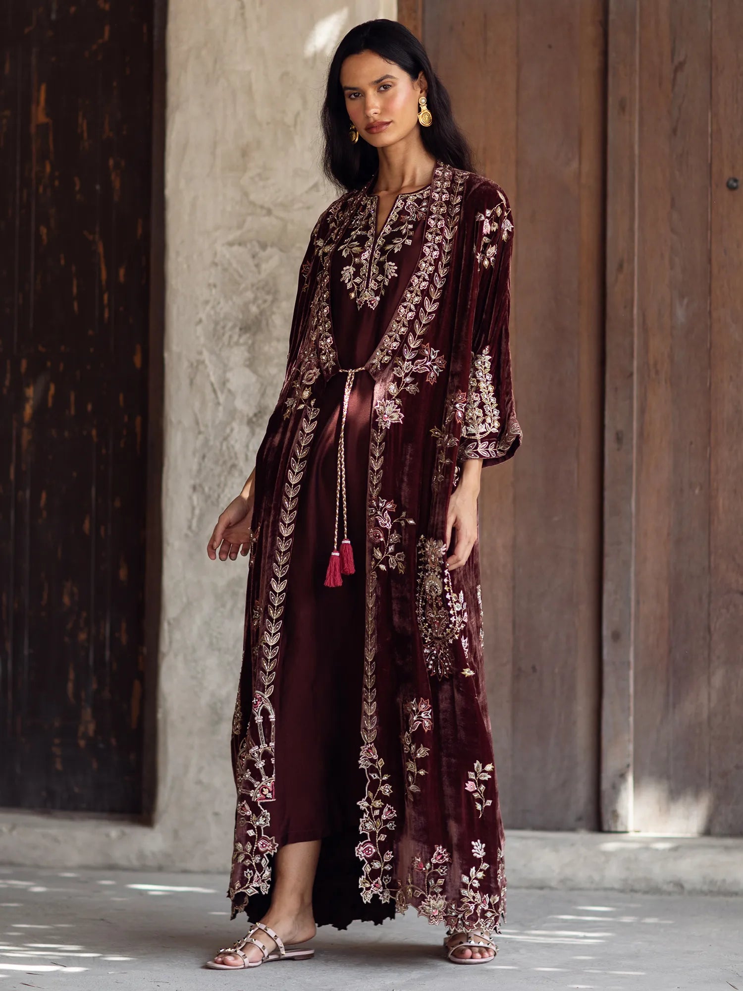 Woman wearing a burgundy embroidered dress with a wooden door in the background