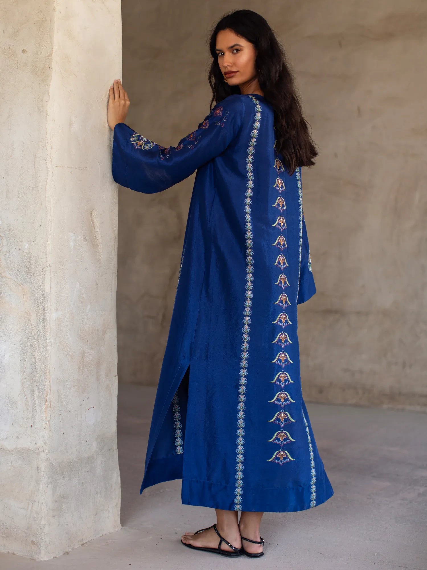 Woman wearing a blue embroidered dress against a neutral wall.