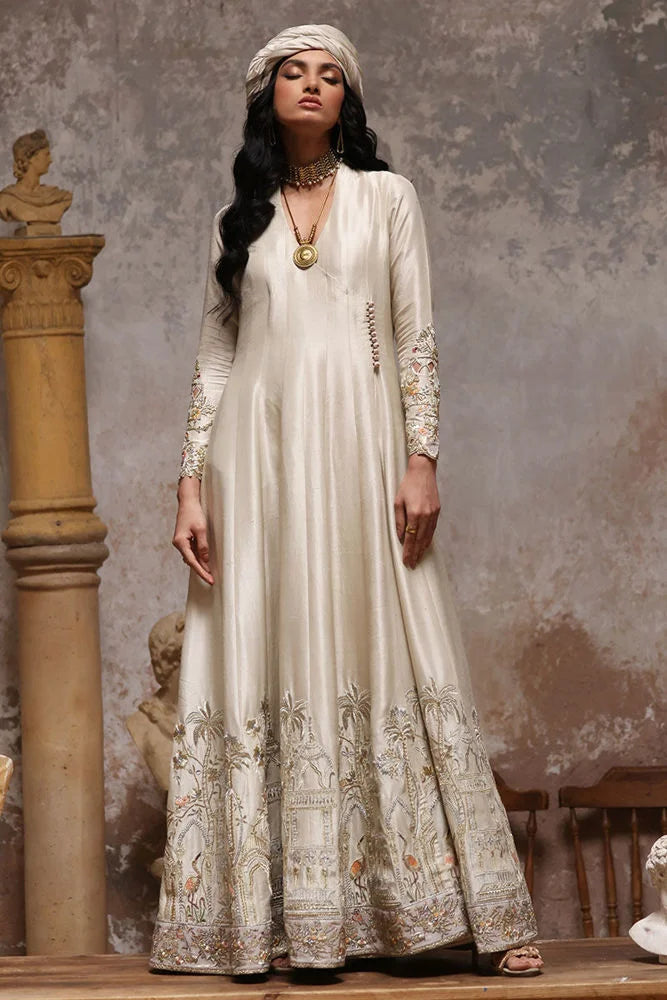 Woman wearing a long, elegant white dress with intricate patterns against a textured wall.