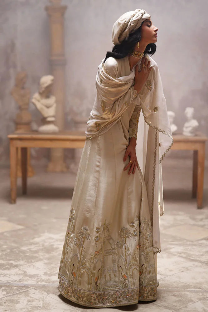 Woman in an elegant, embroidered dress standing in a room with classical sculptures.