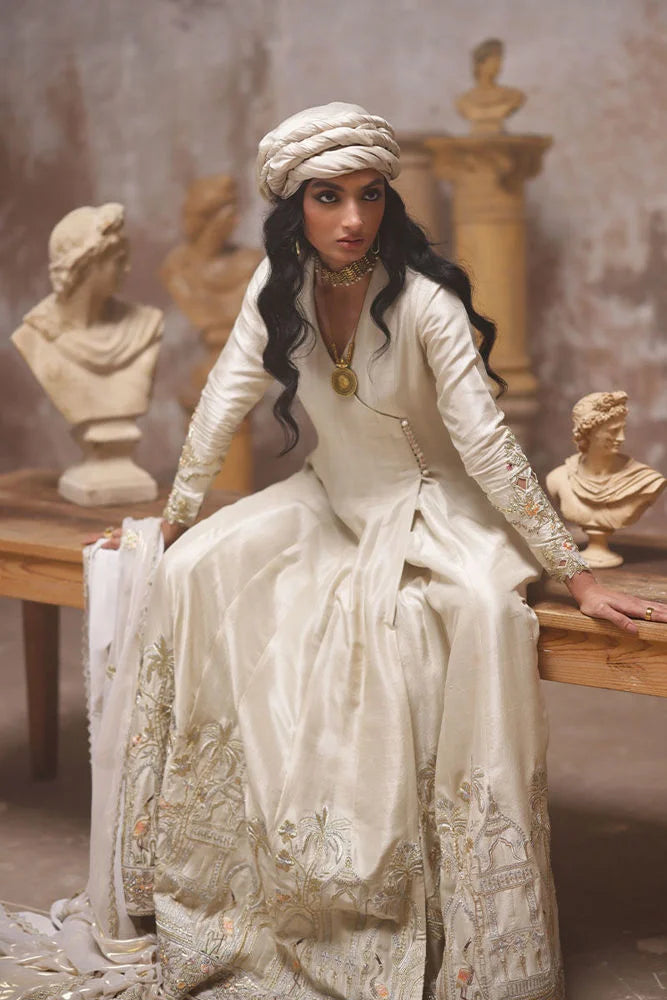 Woman in a white embroidered dress sitting on a wooden bench with classical busts in the background