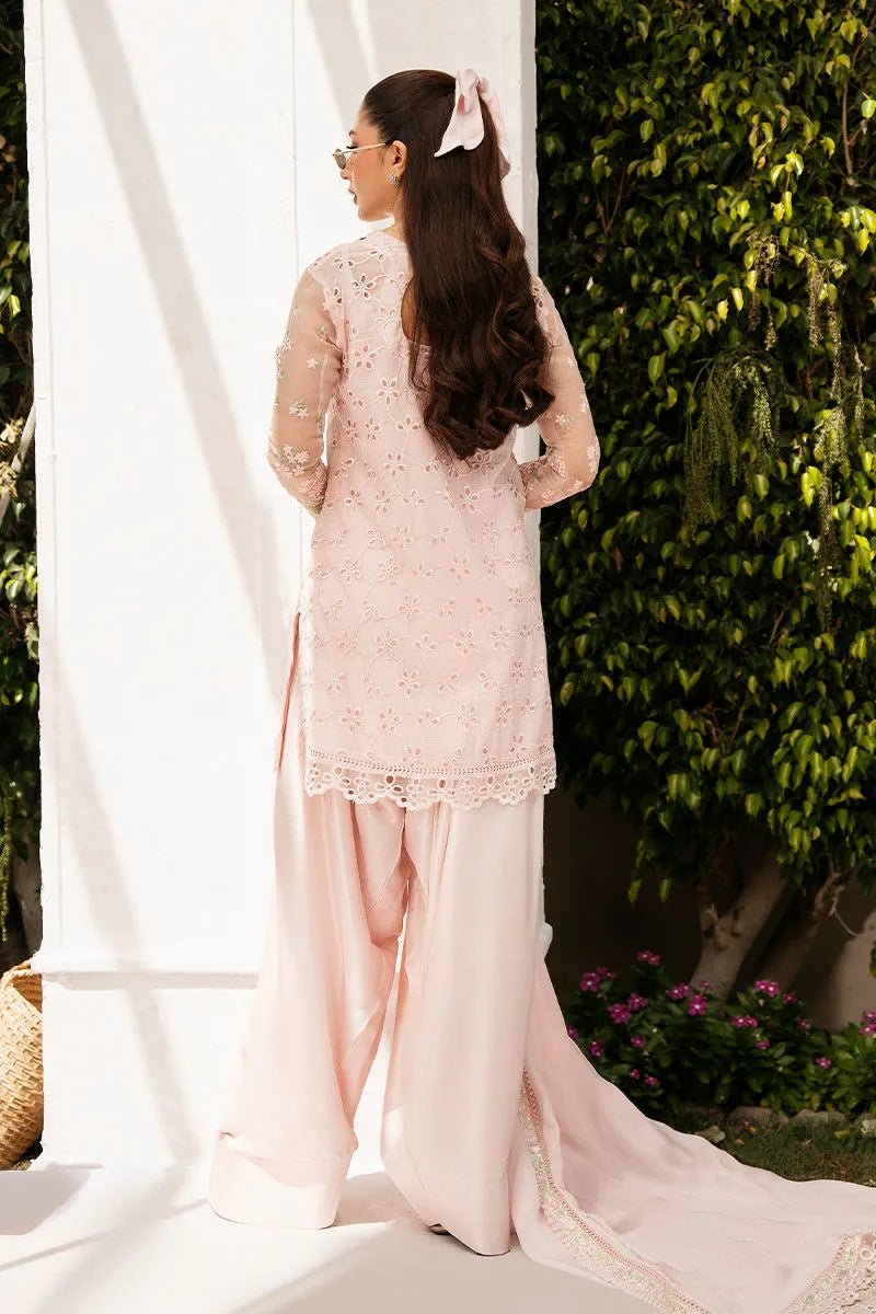 Woman in a light pink traditional outfit standing outdoors with greenery in the background