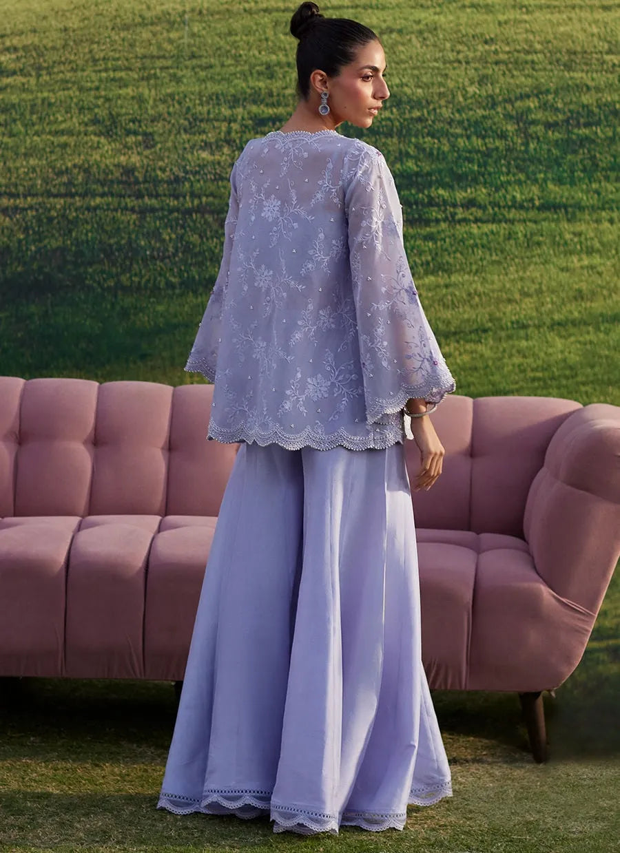 Woman in a light blue outfit standing in front of a pink sofa with a green grass background