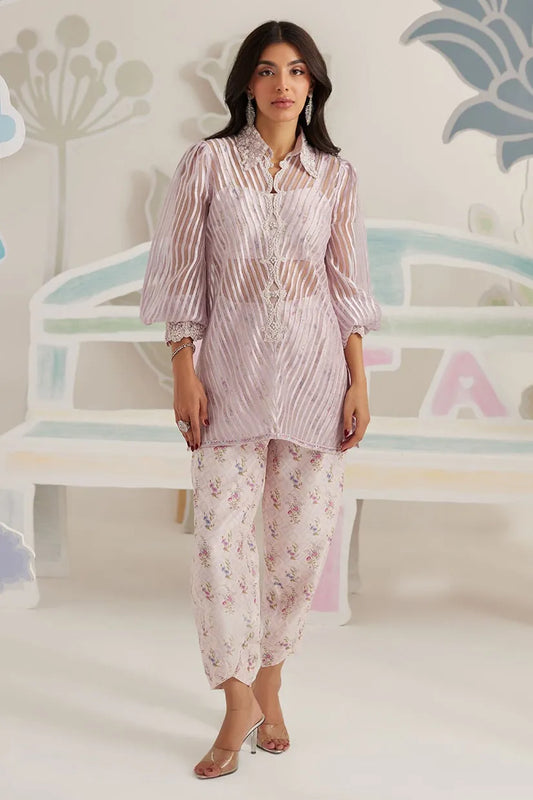 Woman wearing a pink striped outfit with floral pants against a decorative wall.