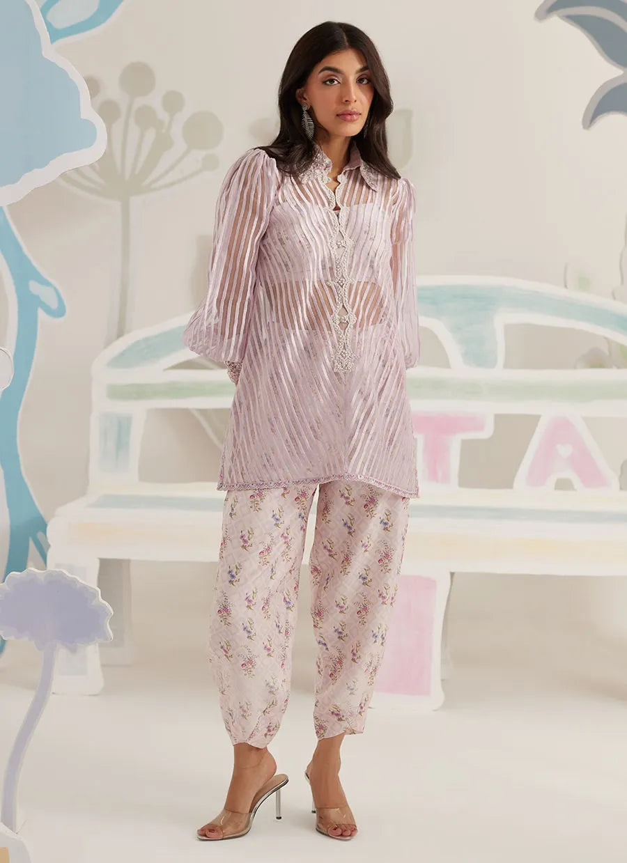 Woman wearing a matching pajama set with floral pants and striped top in a pastel-themed room.