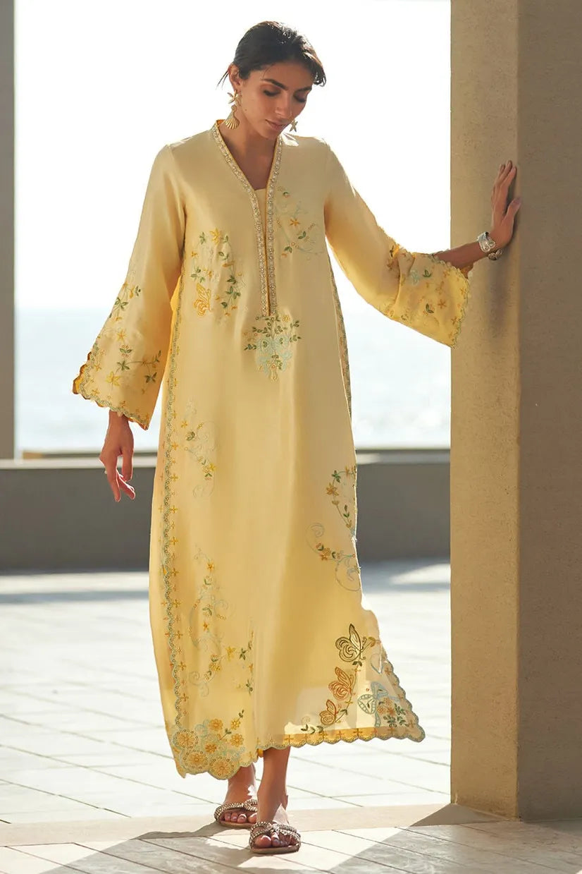 Woman wearing a yellow embroidered dress standing by a columned building.