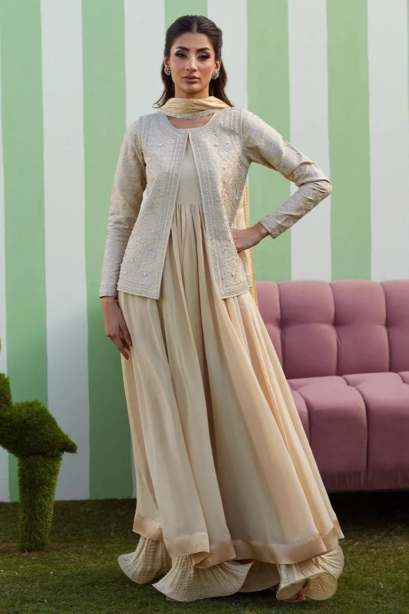 Woman in a beige traditional outfit standing in front of a striped wall with a pink couch.