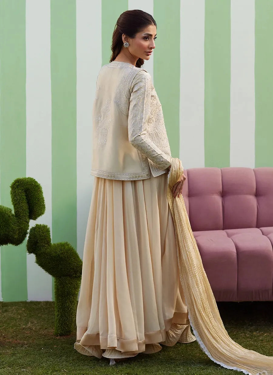 Woman in a beige traditional outfit standing in front of a green and white striped wall with a pink sofa.