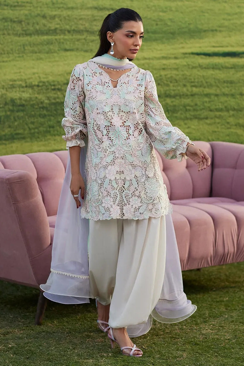 Woman in a floral top and white pants standing in front of a pink sofa with a green grass background