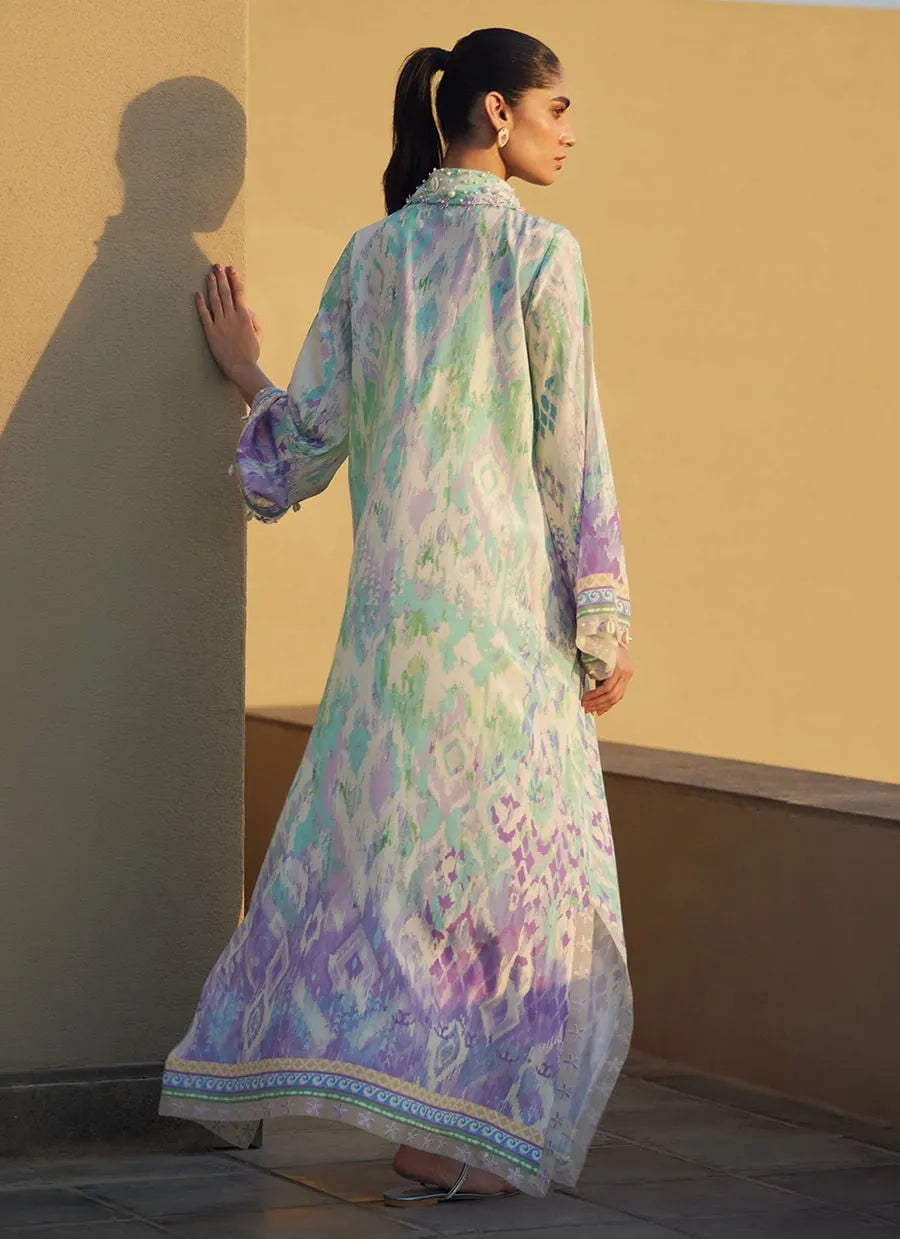 Woman wearing a long, light-colored dress with floral patterns against a beige wall.