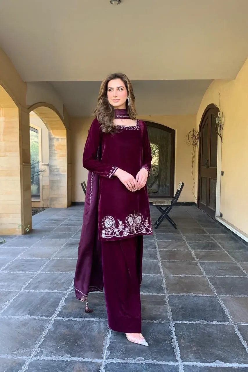 Woman in a burgundy traditional outfit standing in an outdoor setting with stone flooring and archways.