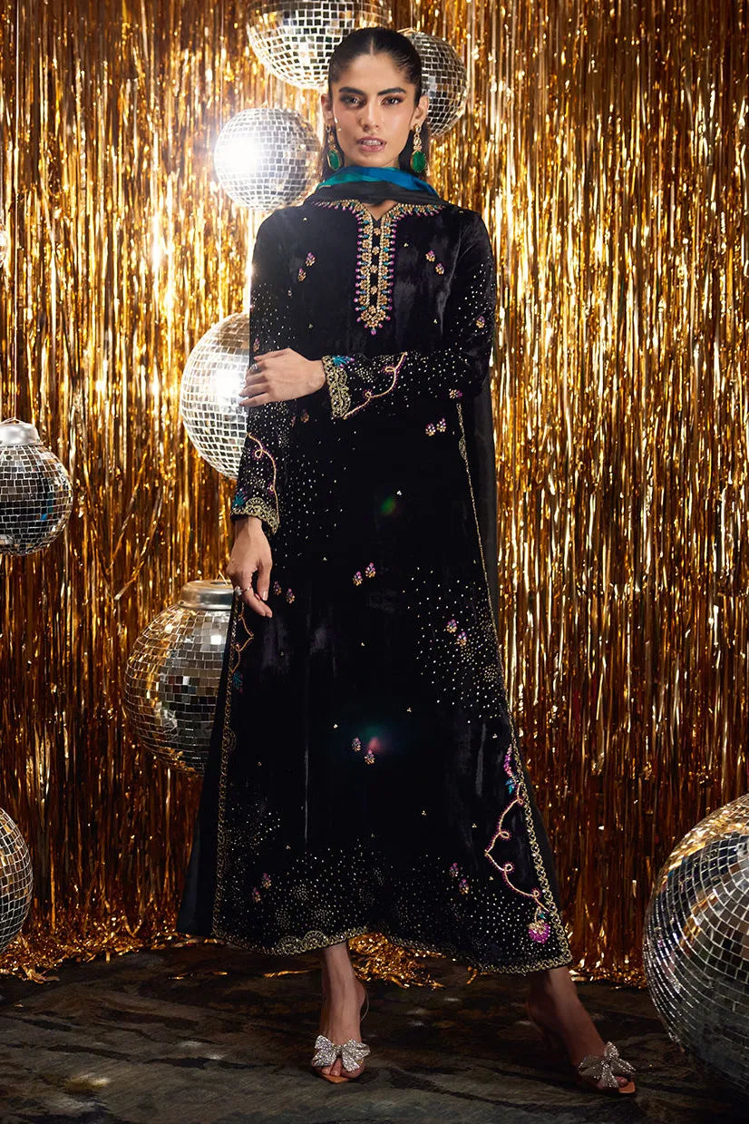 Woman in a black embroidered dress standing in front of a gold curtain with disco balls.
