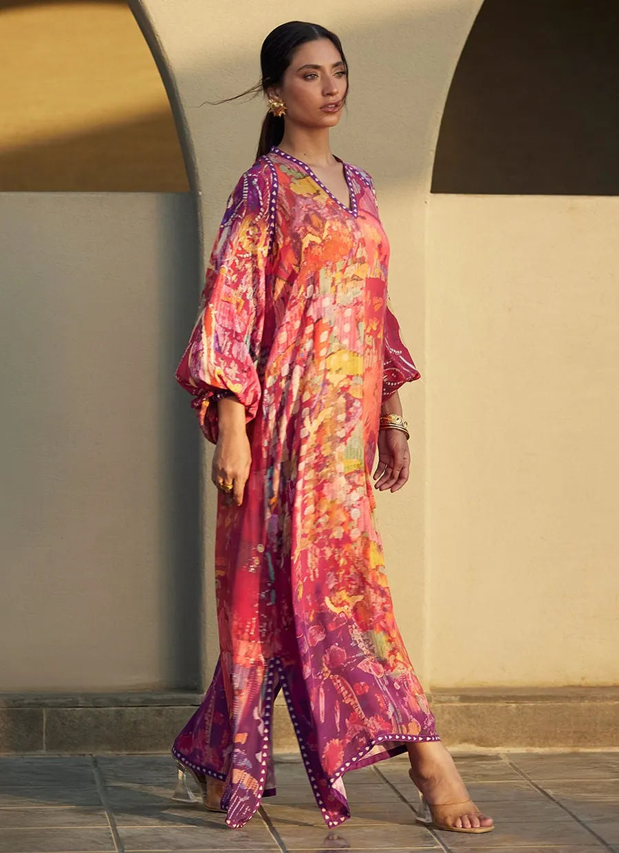 Woman wearing a colorful patterned dress standing against a neutral wall.