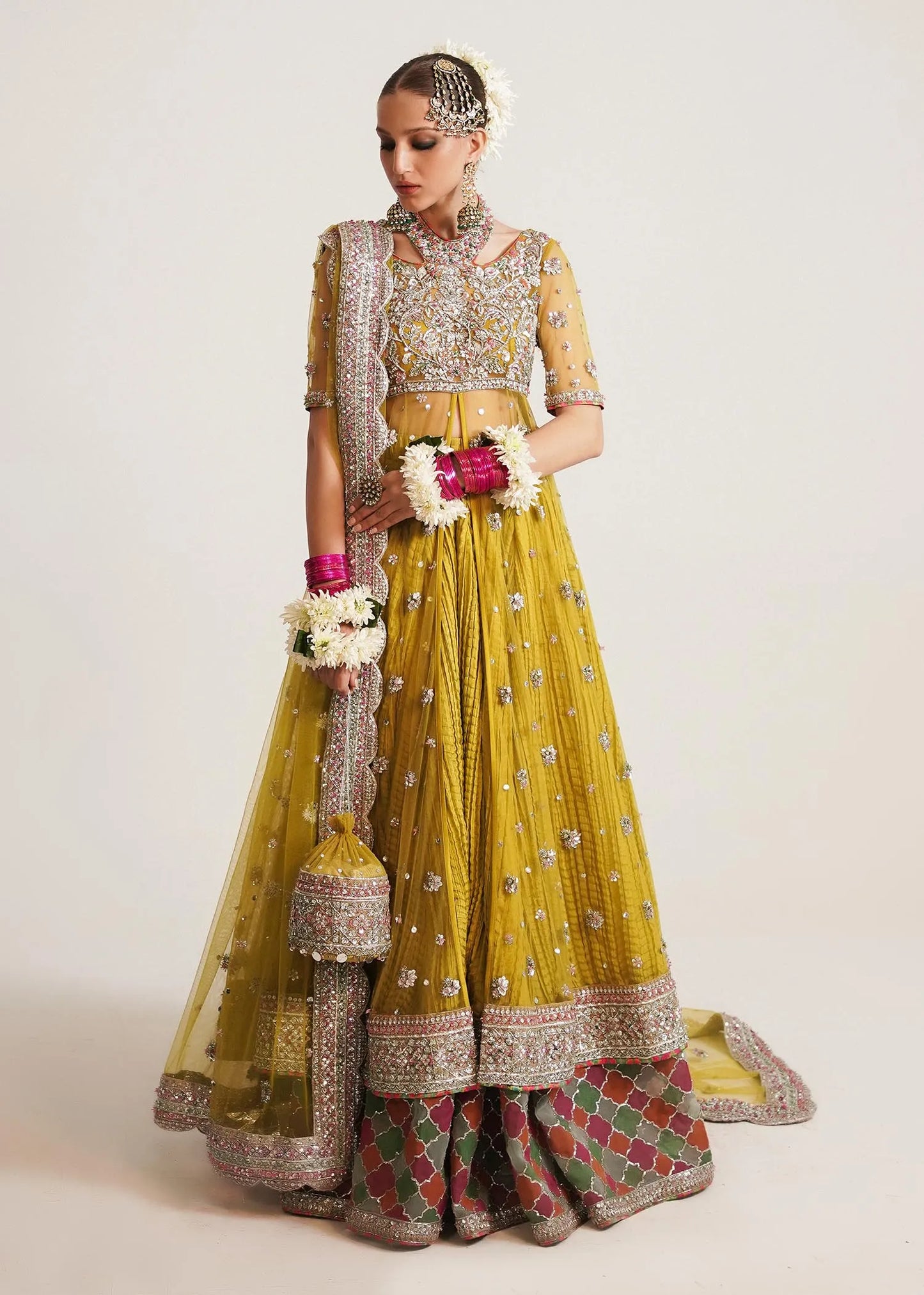 Woman in a traditional yellow and green outfit with jewelry and flowers on a white background